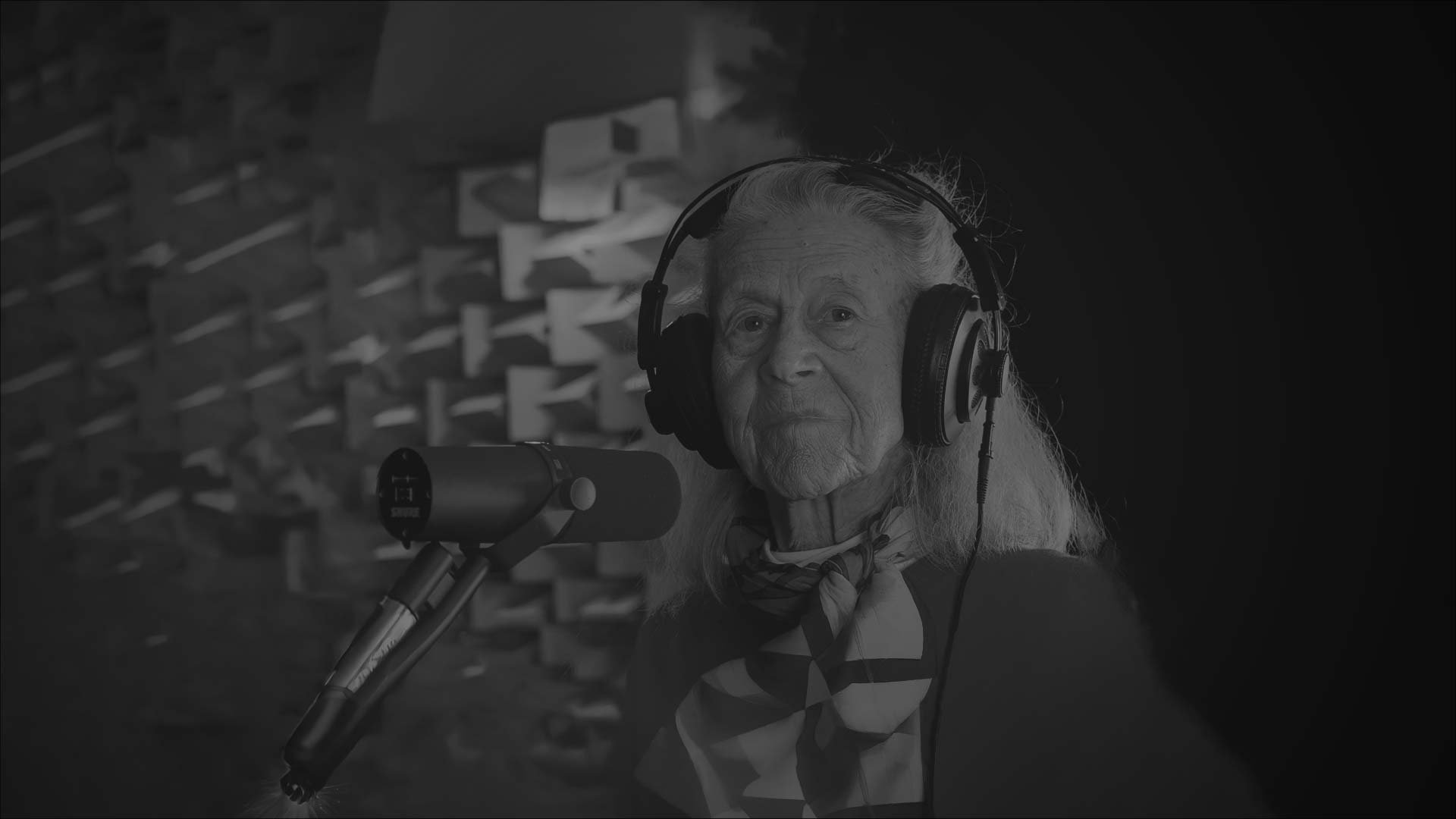 An older woman wearing headphones in a recording studio.