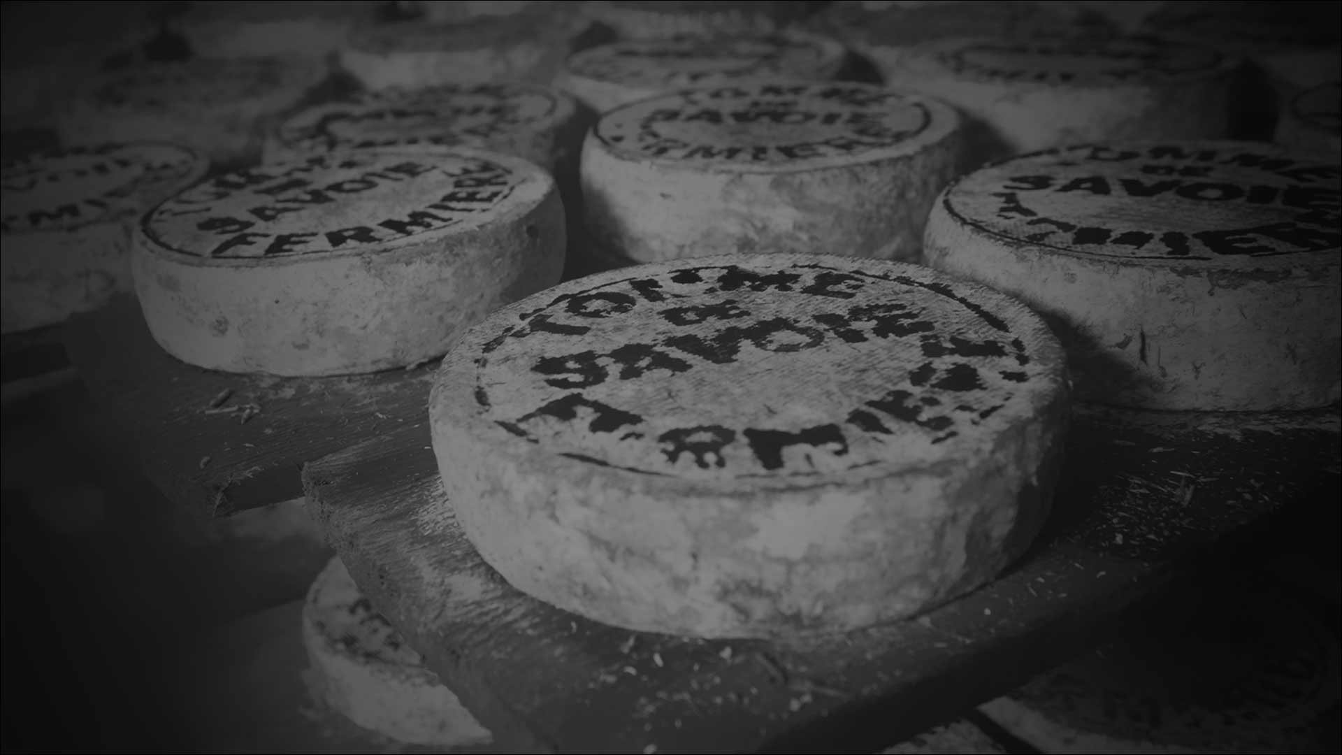 Stacks of round cheese wheels with stamped labels, resting on wooden shelves.