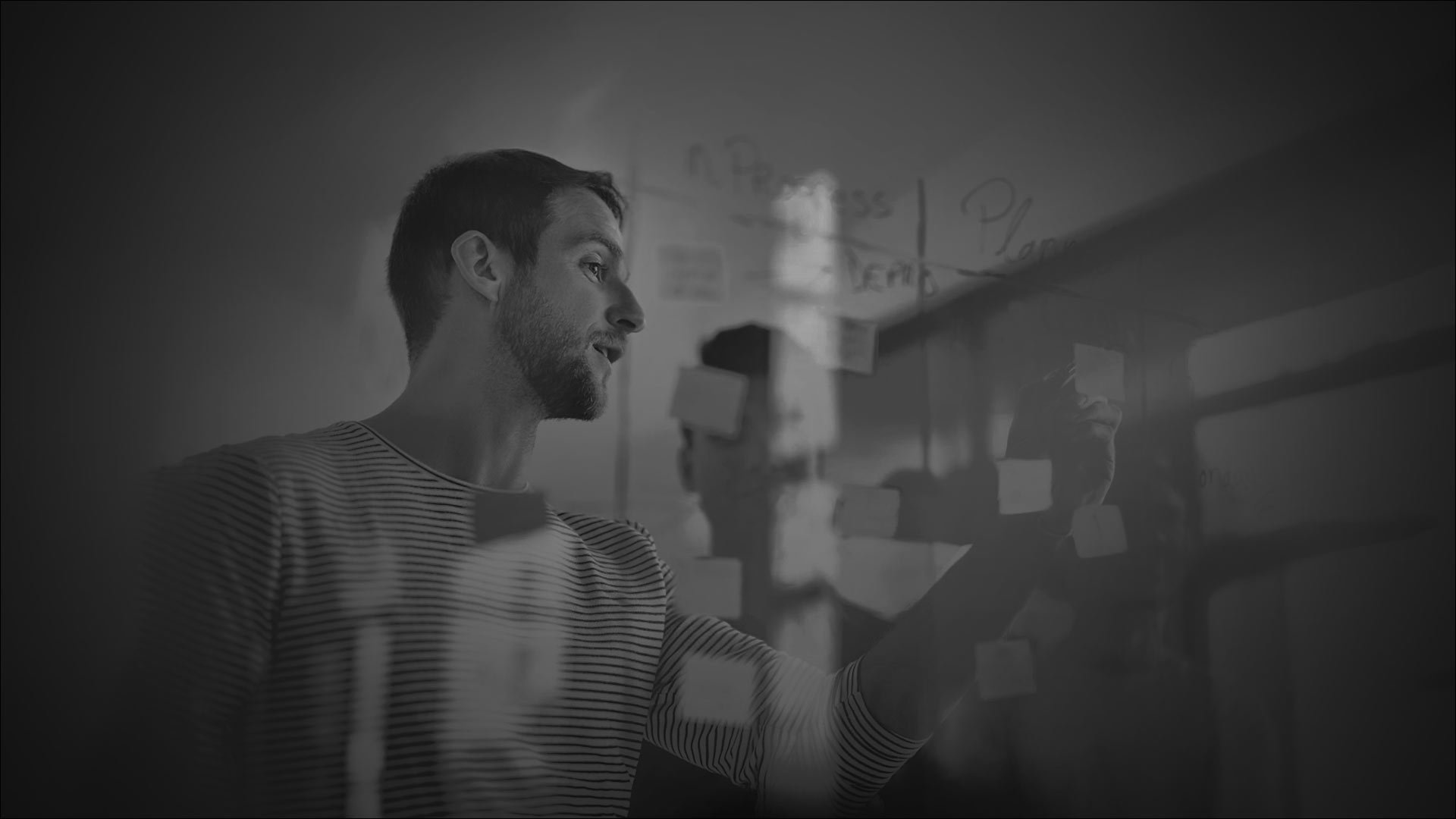 A man stands in front of a wall, observing a portrait of a man displayed on it.