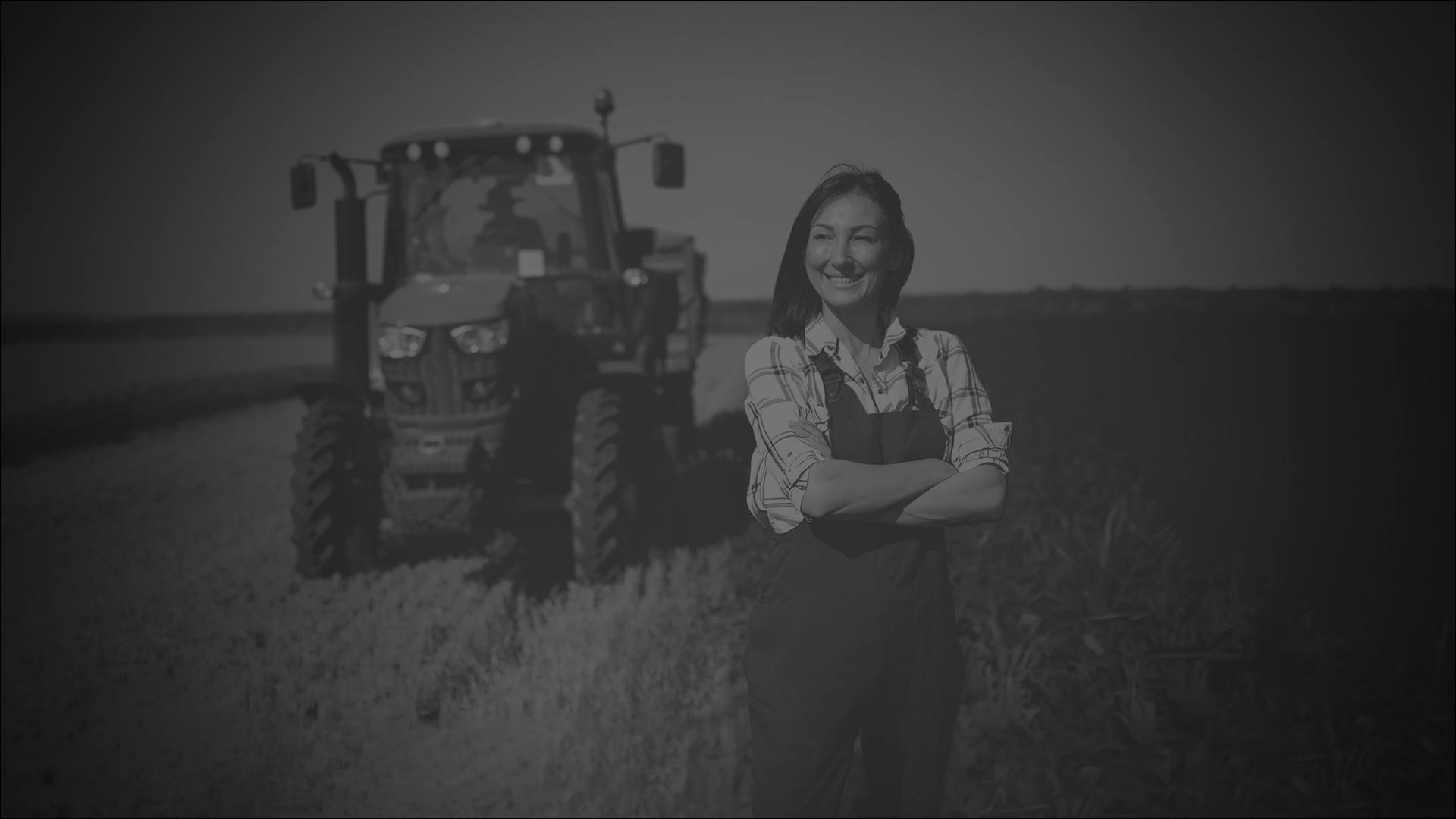 A woman stands in a field beside a tractor, surrounded by green crops under a clear blue sky.